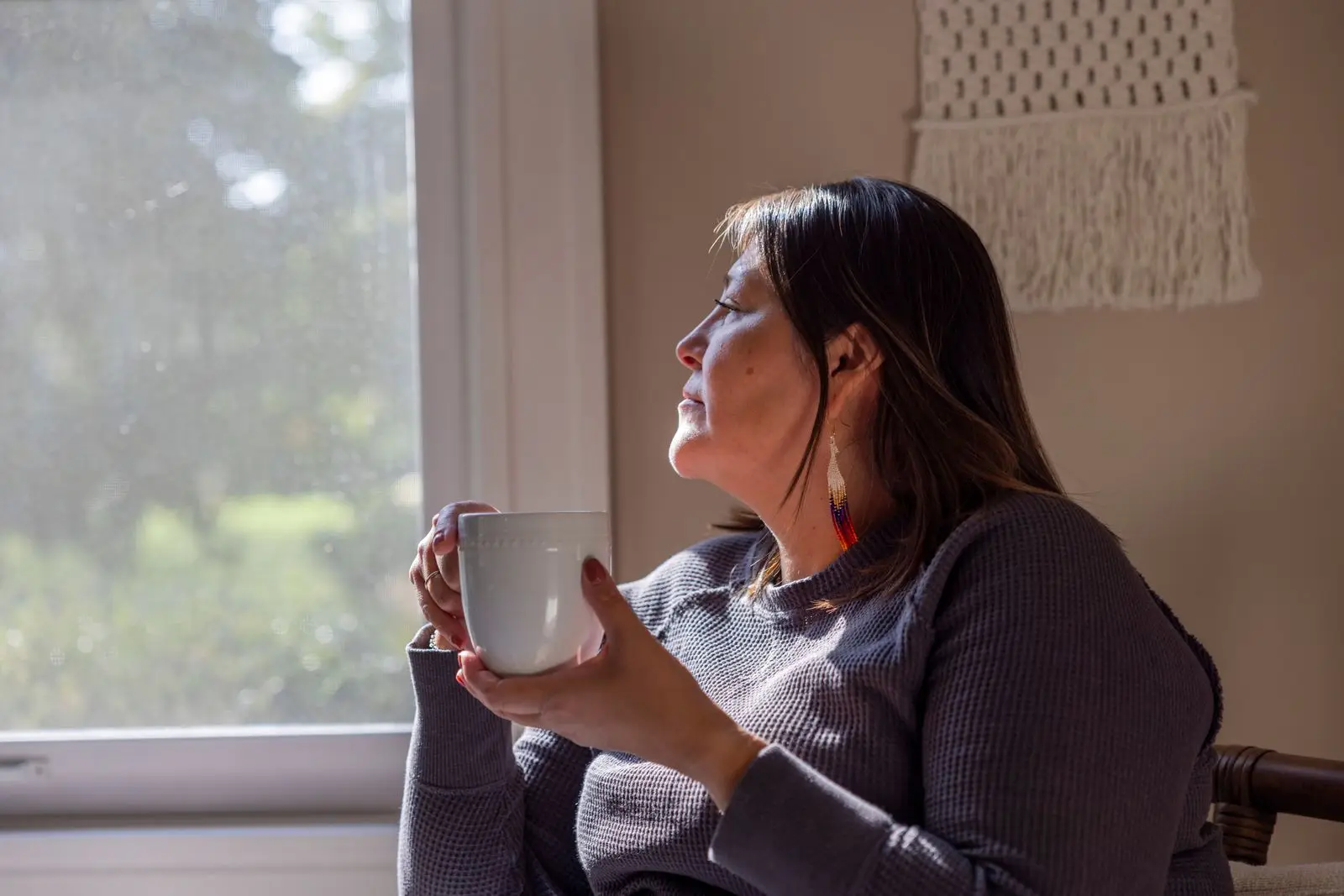 Nachdenkliche Frau mit Tasse am Fenster